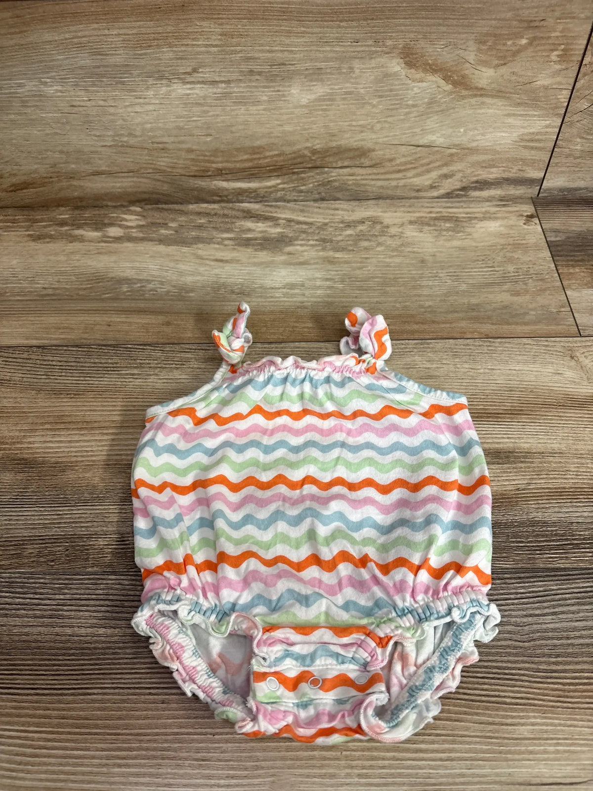 Top view of Old Navy bubble romper in white with wavy rainbow stripes, tie shoulder straps and snap crotch on wood background