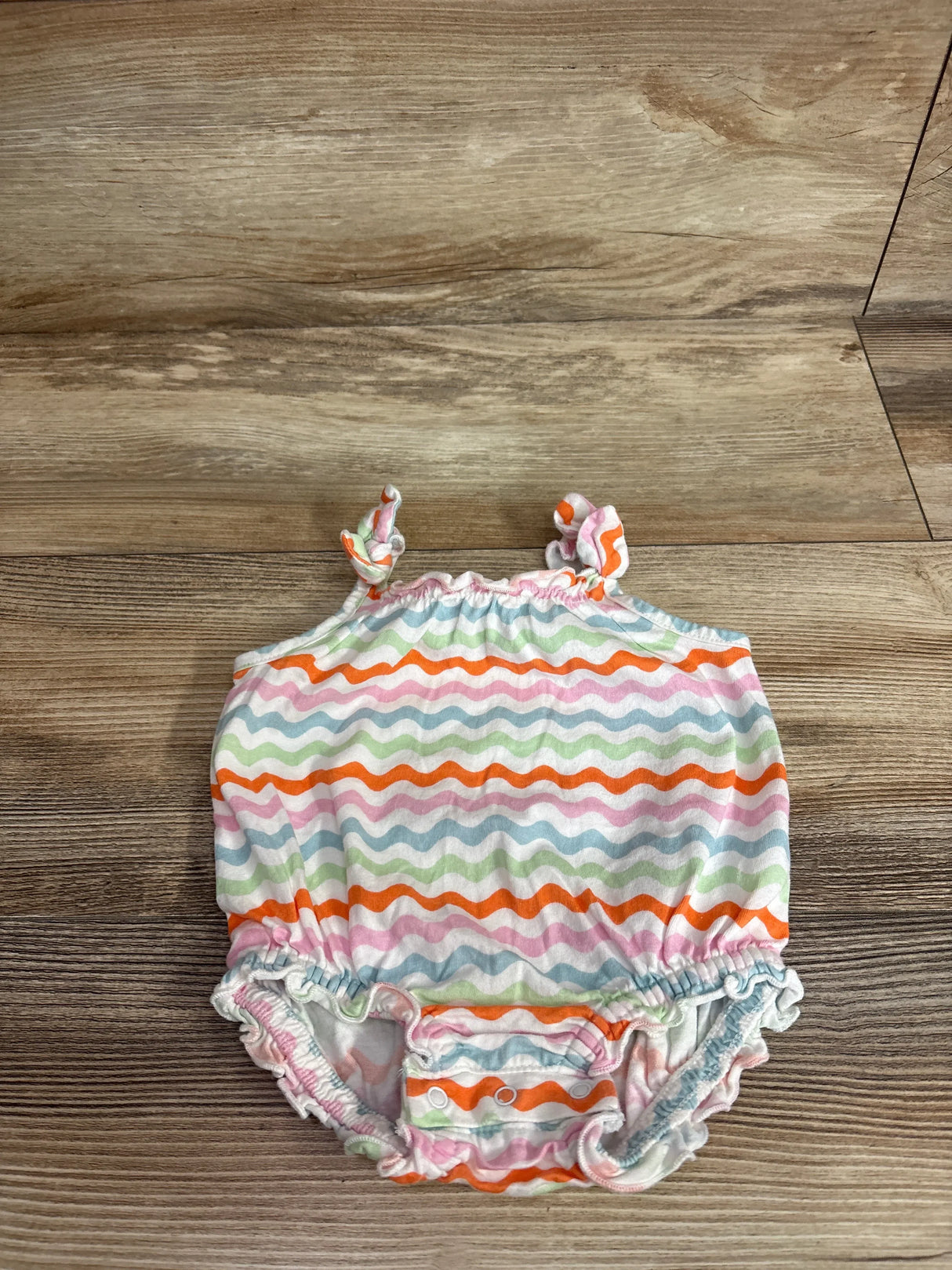 Top view of Old Navy bubble romper in white with wavy rainbow stripes, tie shoulder straps and snap crotch on wood background