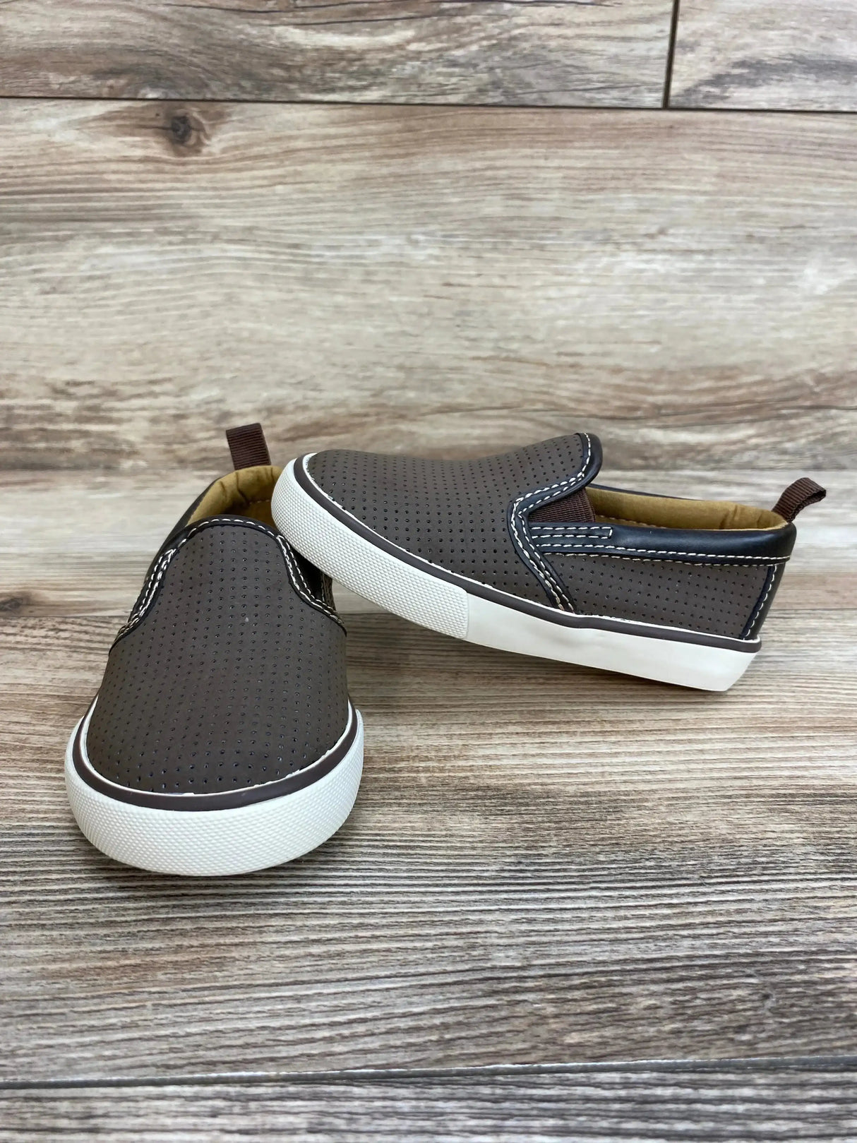Three-quarter view of Gap toddler slip on sneakers brown size 6c showcasing perforated upper white sole and elastic side gores on wood plank floor
