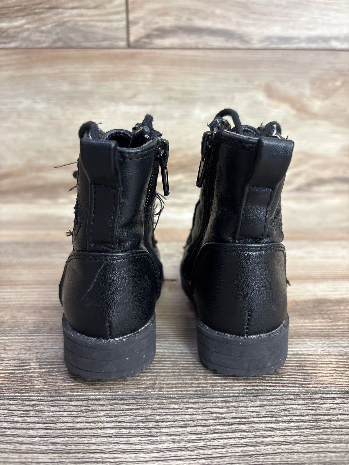 Rear view of Sugar faux leather butterfly boots in black showcasing back zippers and pull tabs on wood floor
