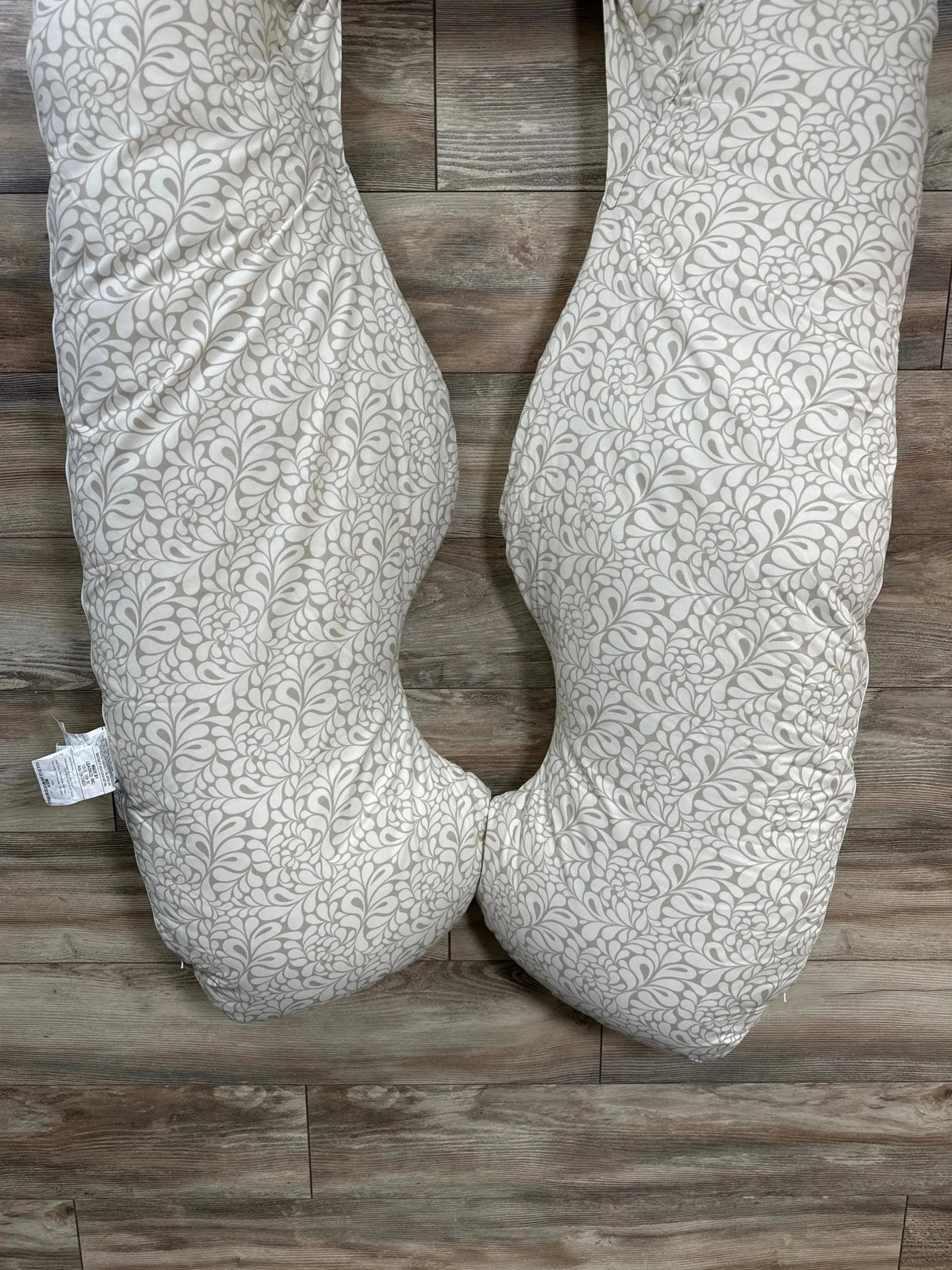 Top-down view of Leachco Back 'N Belly U-shaped maternity pillow showing taupe Chic Splash floral cover on wood floor