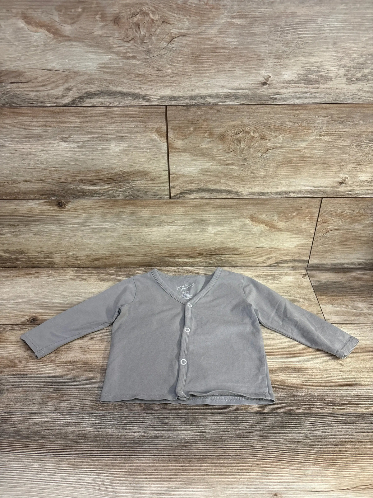 Flat-lay of grey button-front baby shirt showing long sleeves and three front snap buttons on wood plank background