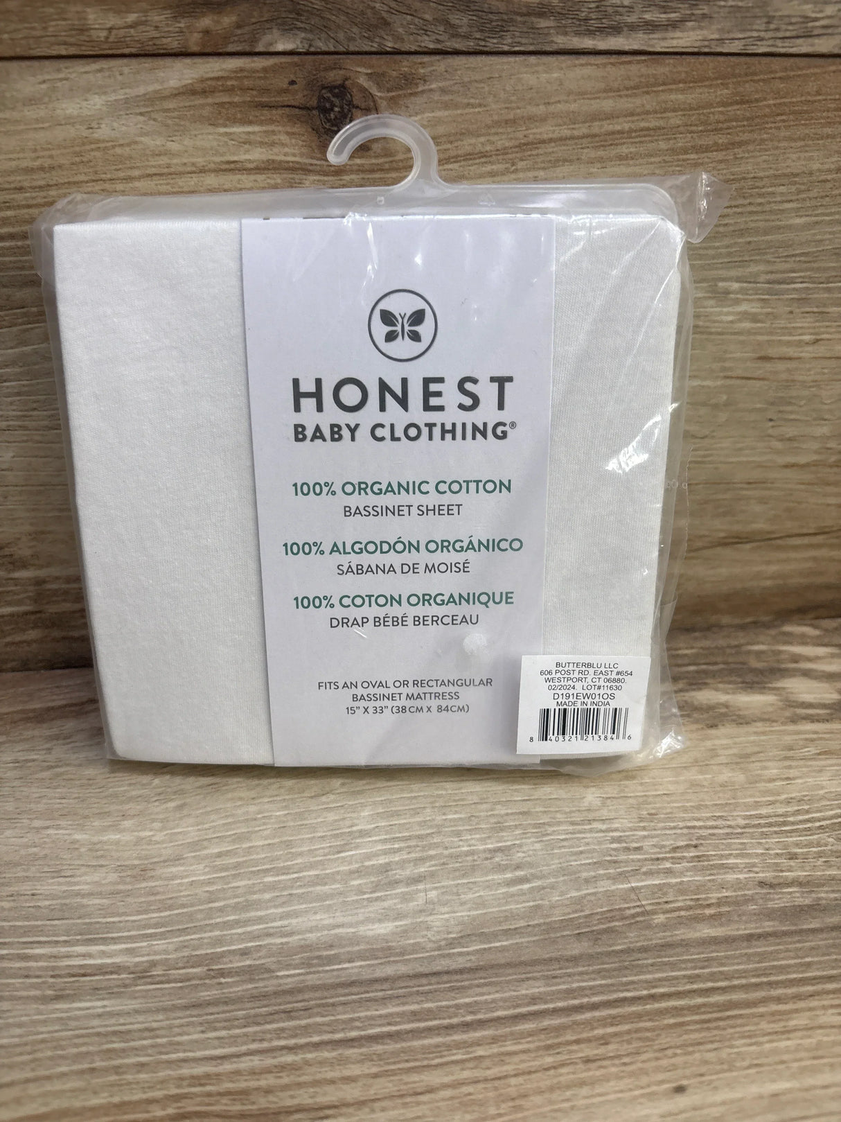 Front view of Honest Baby white bassinet sheet showing packaging label 100 percent organic cotton on wood background