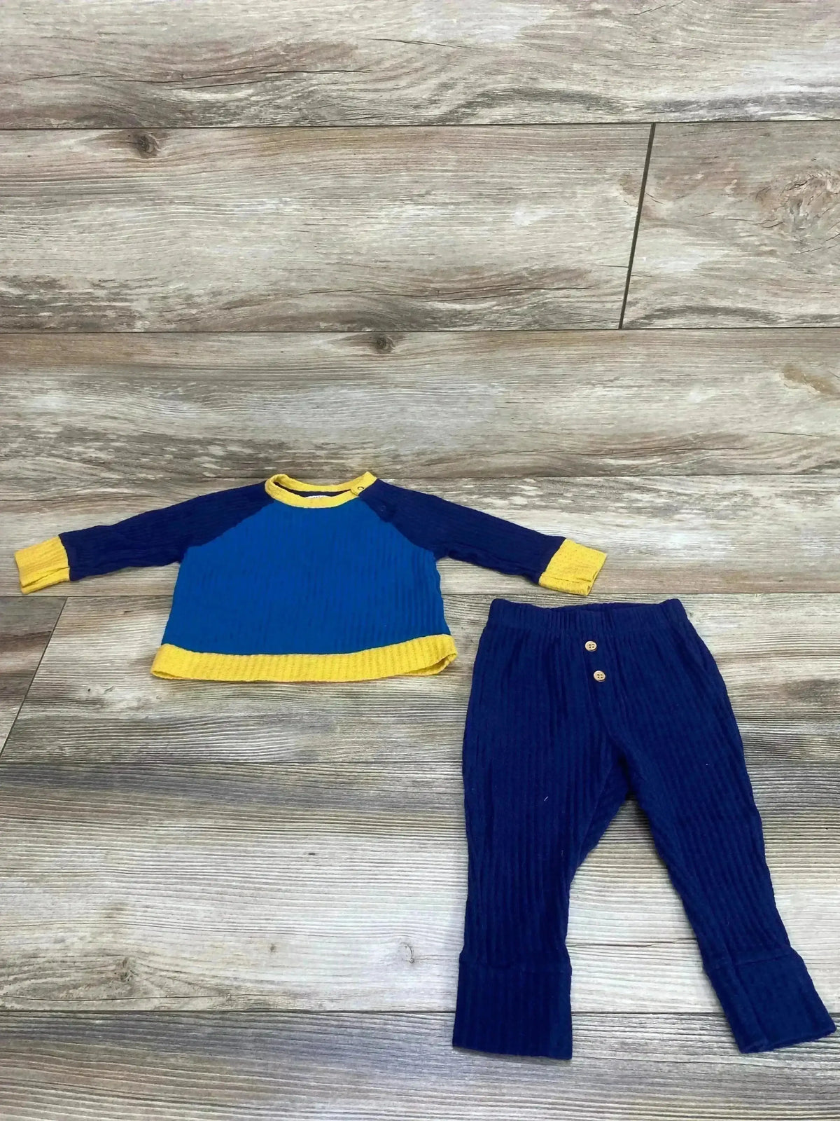 Top-down view of Cat & Jack navy waffle-knit long-sleeve shirt and pants set with yellow trim showing ribbed texture on wood floor