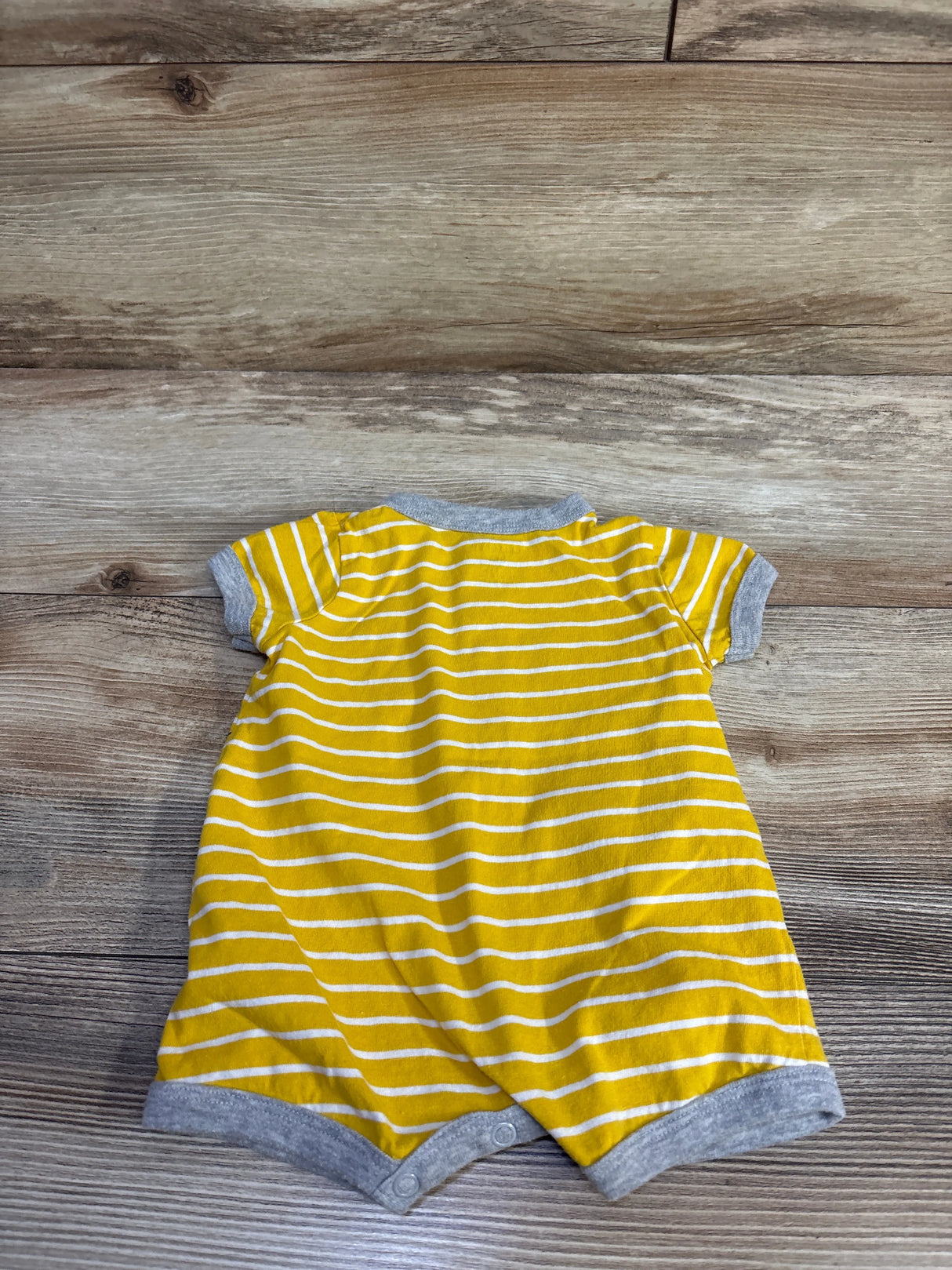 Back view of yellow and white striped baby shortie romper showcasing gray trim and snap crotch on wooden background