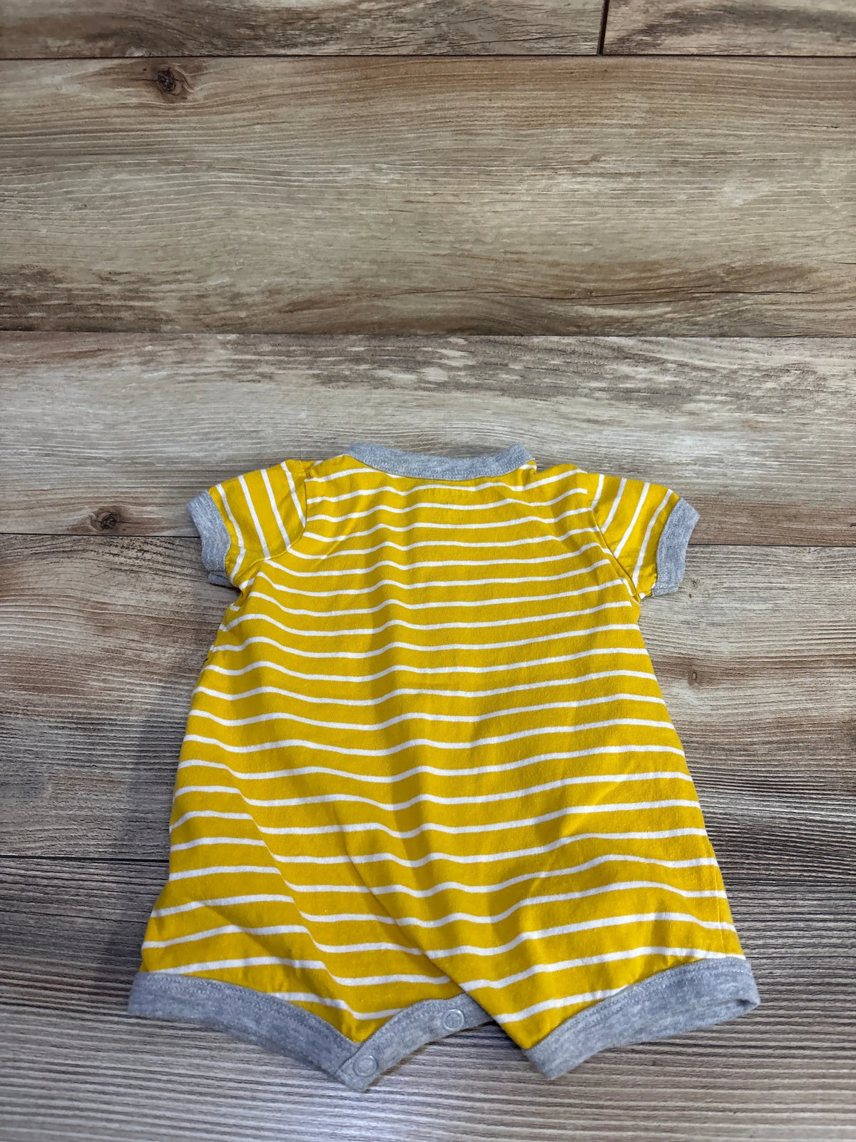 Back view of yellow and white striped baby shortie romper showcasing gray trim and snap crotch on wooden background