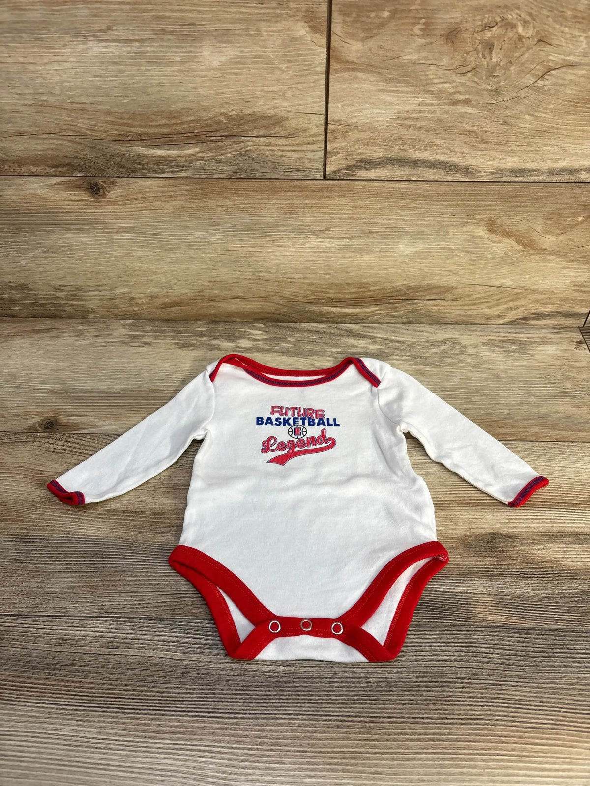 Flat lay of white long-sleeve size 3M bodysuit with red trim, Future Basketball Legend print and snap crotch on wood background