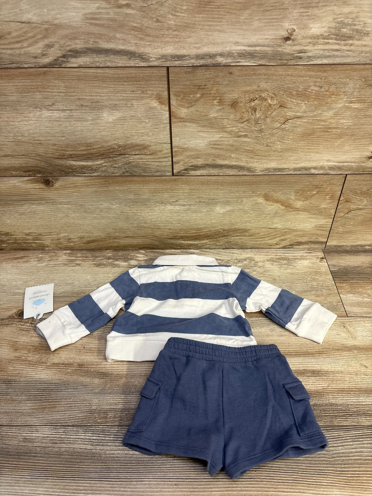 Cloud Island 2-piece baby set with blue and white striped polo and blue shorts on a wood background