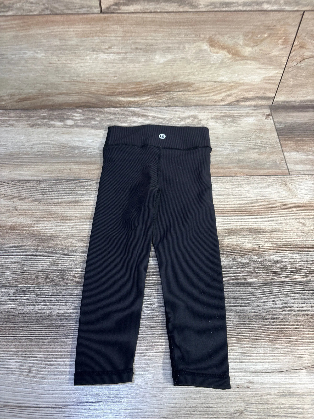 Front view of Little Bipsy Active Ribbed Leggings in black showcasing ribbed texture and wide waistband on a wood-look floor