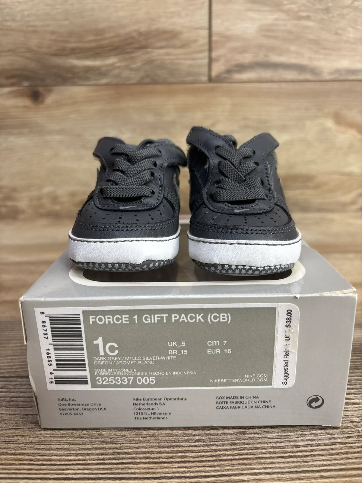 Dark grey infant Nike sneakers with laces on box, labeled Force 1 Gift Pack size 1C