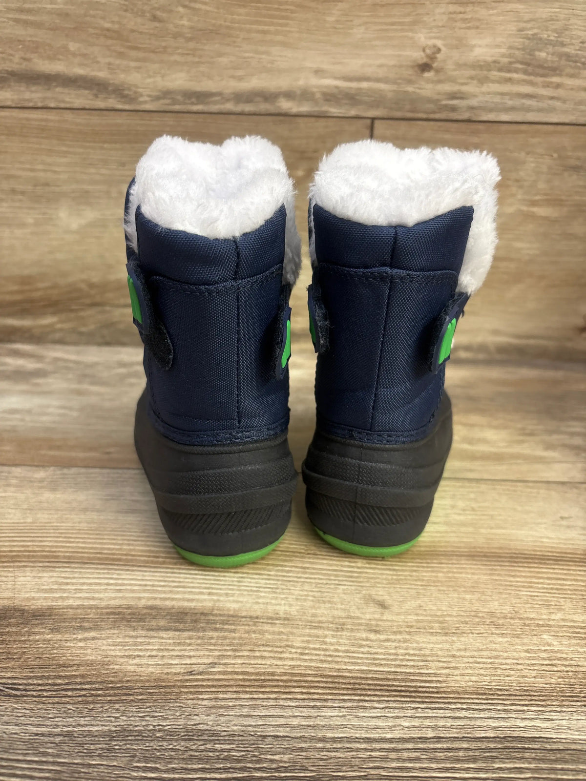 Rear view of Morendl winter snow boots in navy with white plush lining green accents and black soles on wood flooring