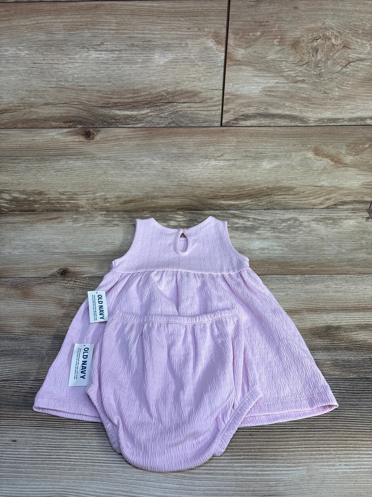 Flat-lay view of pink two-piece baby dress and bloomers set showcasing crochet panel with wood-grain background