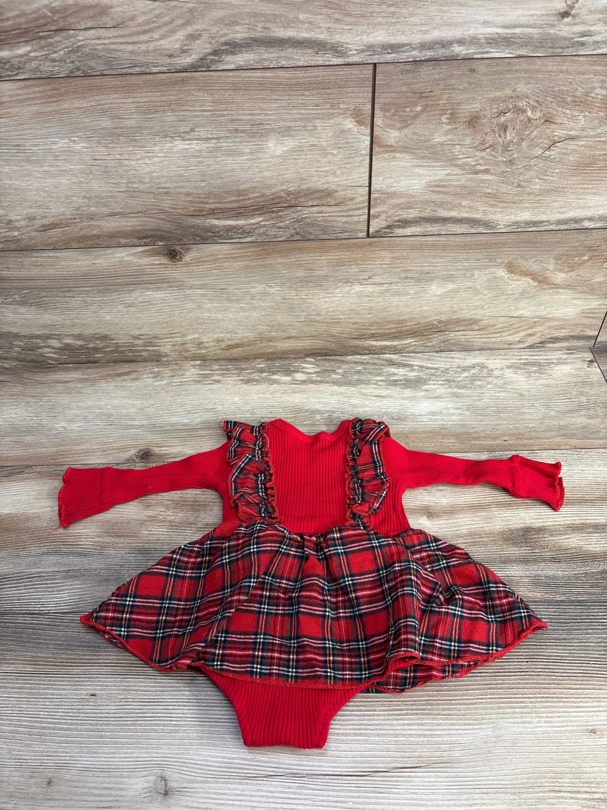 Red infant long sleeve plaid dress romper with ruffle details on a wood background