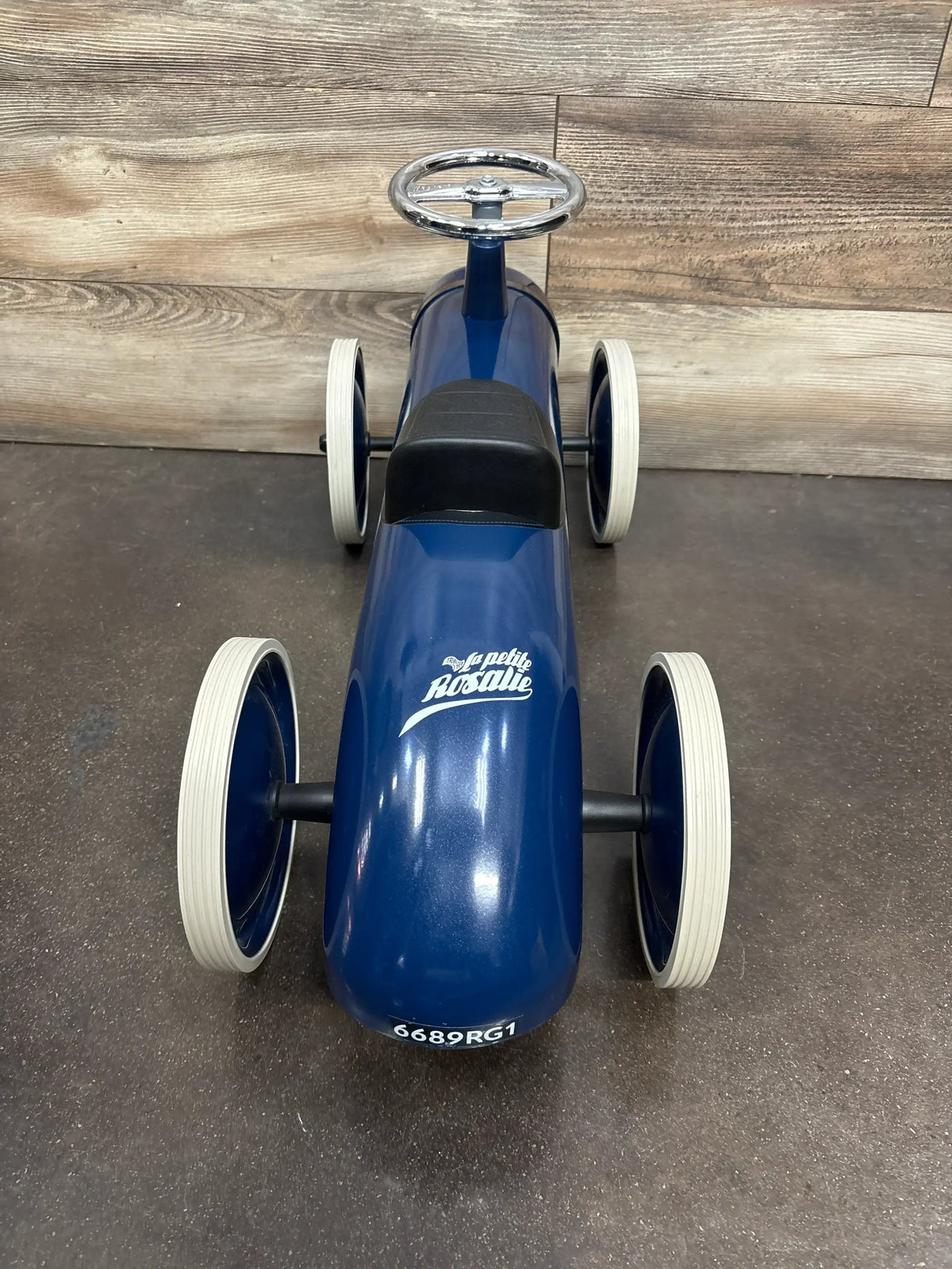 Front view of Baghera Speedster Rosalie ride-on in glossy blue showing white wheels, black seat, and chrome steering wheel on wood floor