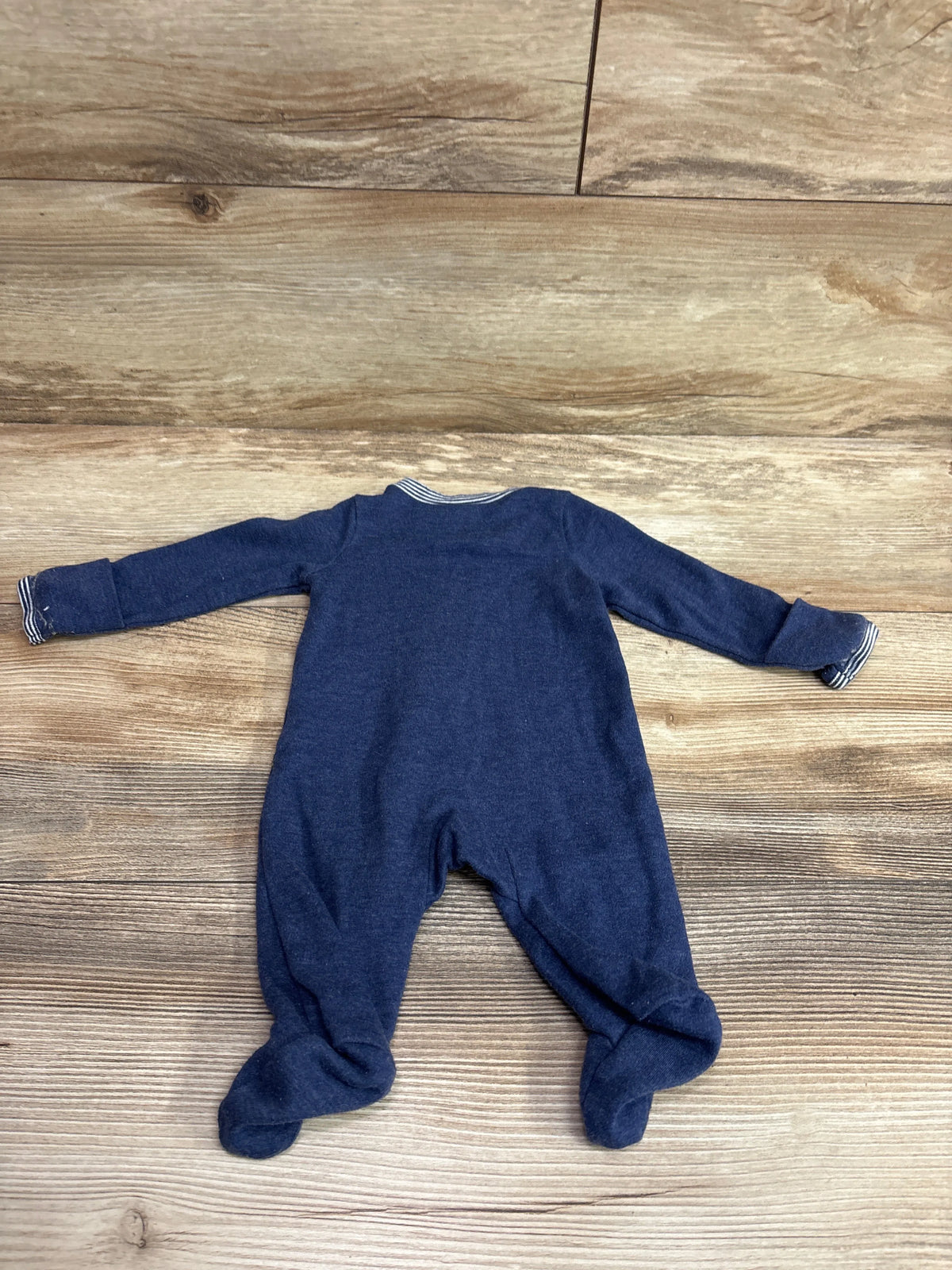 Flat lay of Carter’s blue newborn sleeper showing long sleeves and covered feet on a wood-look background