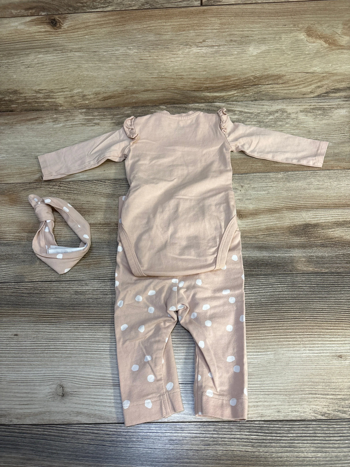 Peach polka dot baby romper and matching headband on wood background