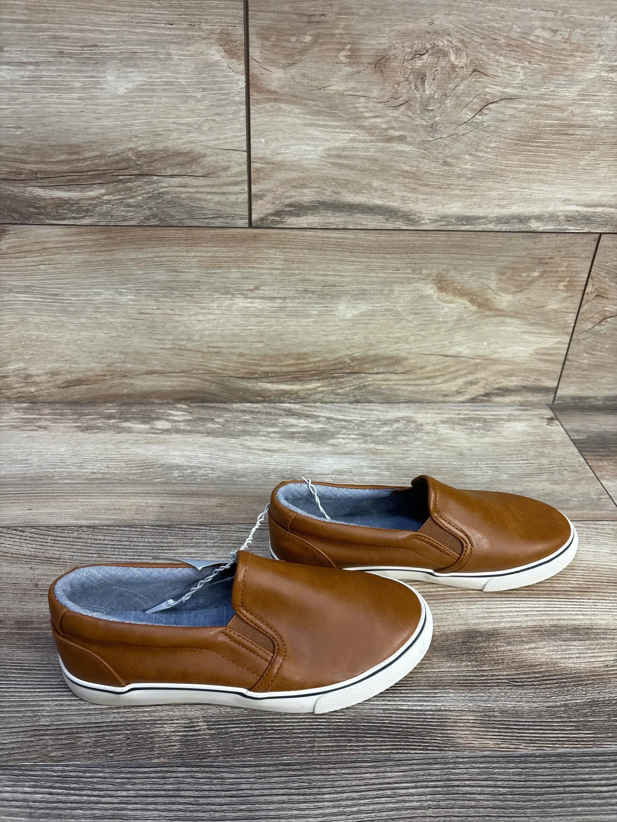 Side view of brown toddler Cat and Jack slip on sneakers with faux leather upper and white rubber sole on wood background
