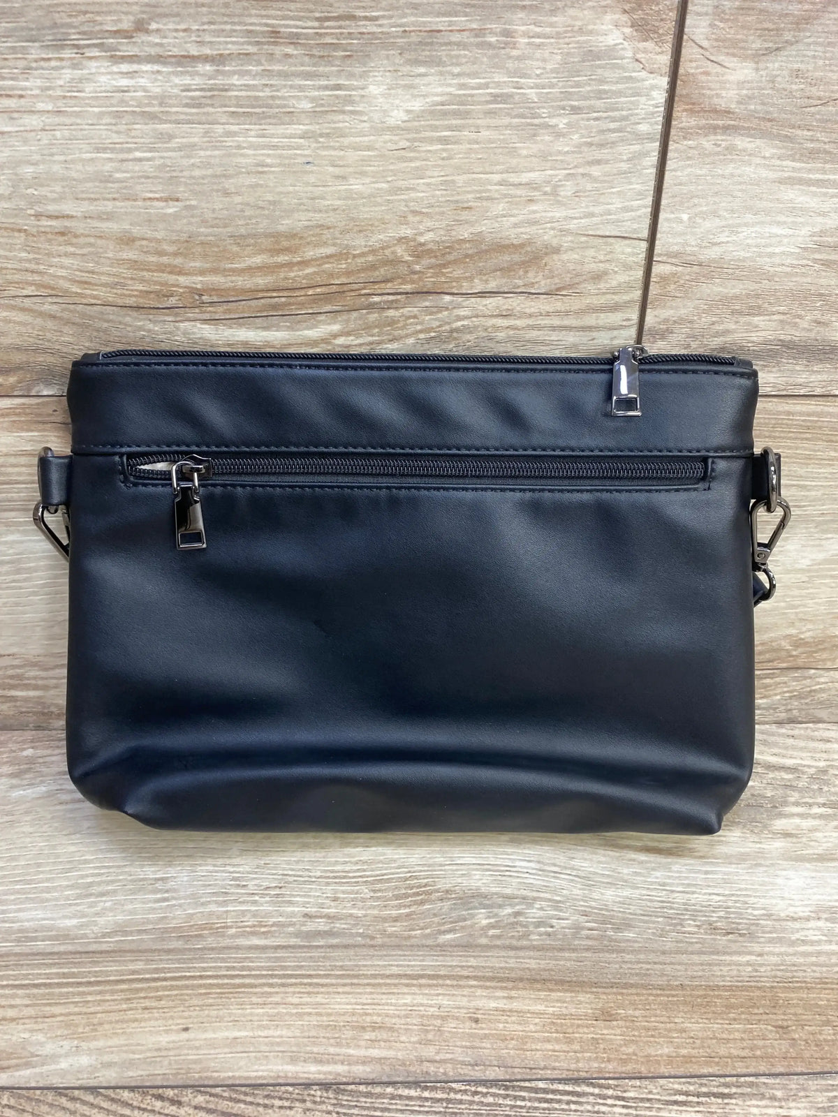 Front view of Brite Tools Leather Diaper Clutch in black with front zip pocket top zip closure and side strap loops on wood plank floor