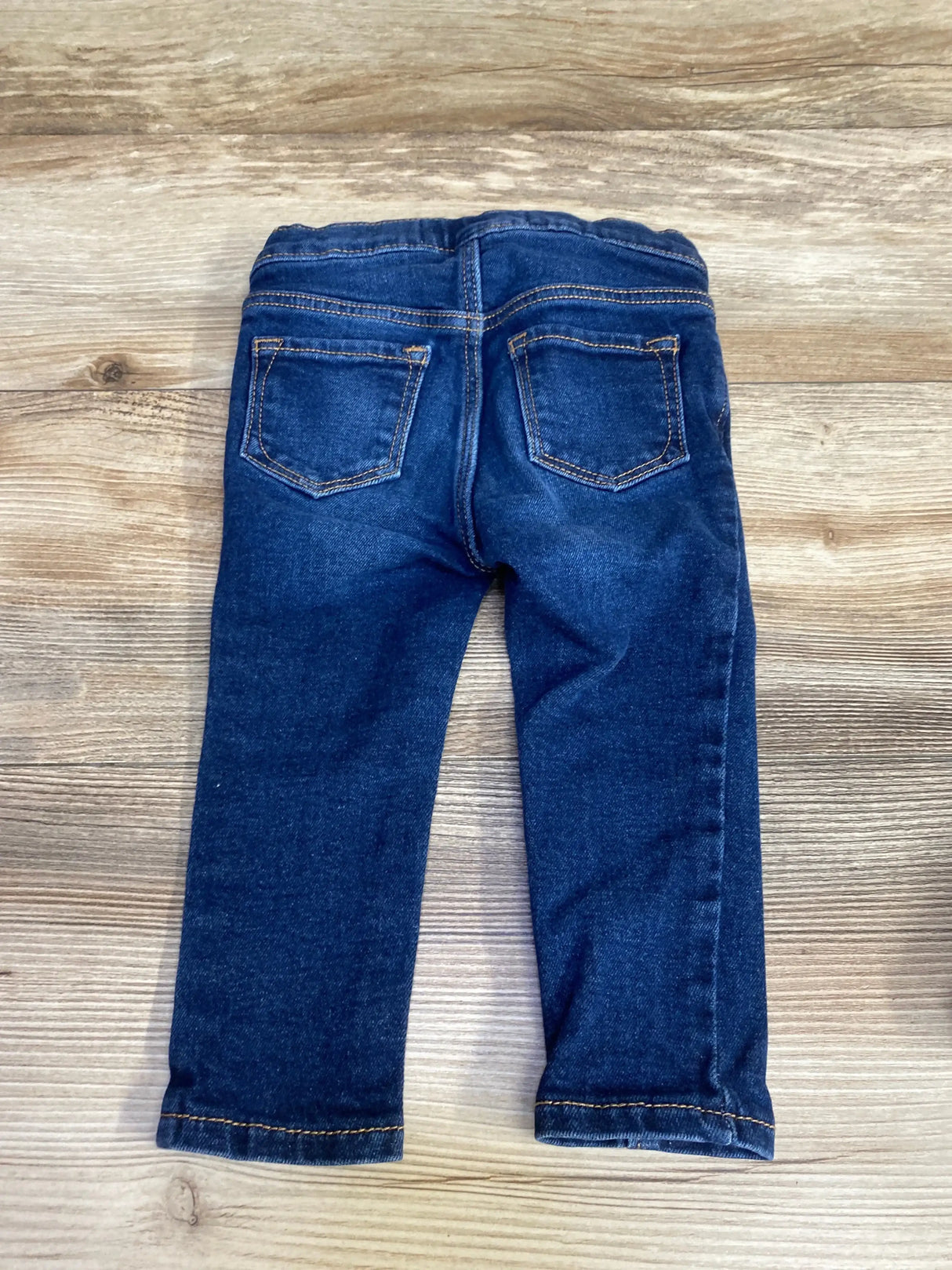 Back view of toddler blue Old Navy skinny jeans showcasing two back pockets and elastic waistband on wood floor background