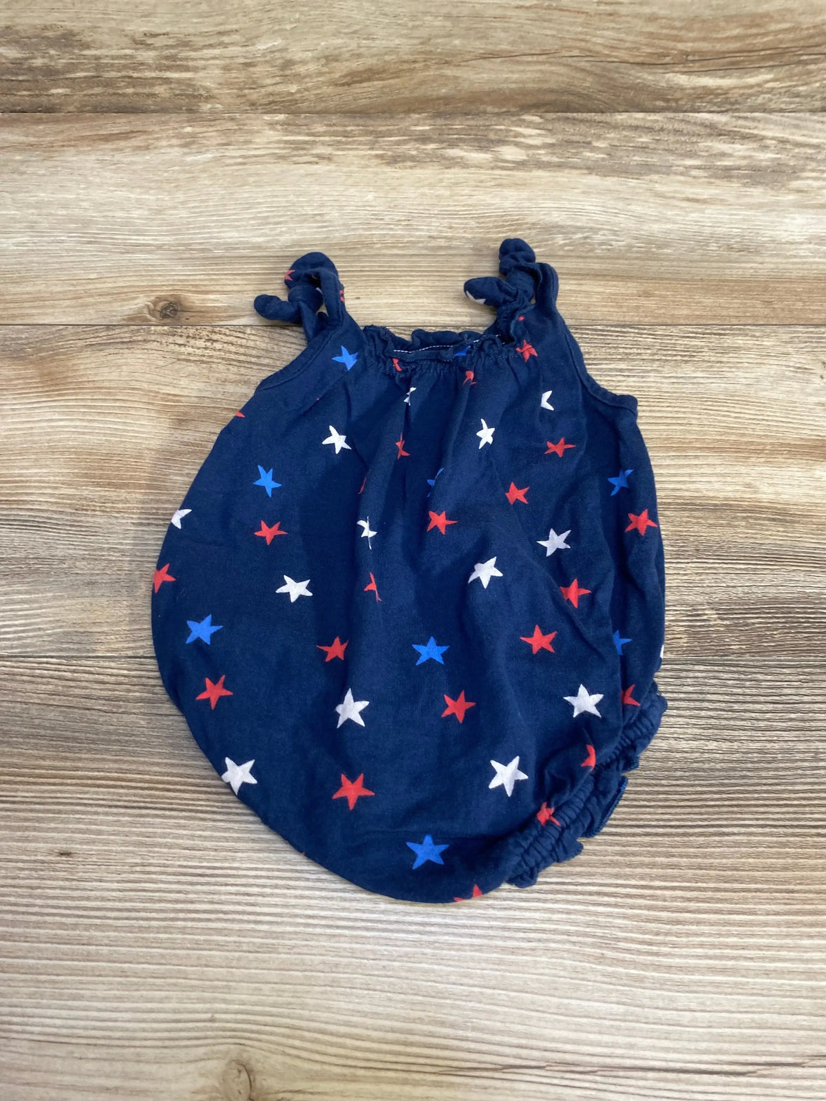 Top-down view of newborn navy star-print romper with knotted shoulder straps and elastic leg openings on wood background