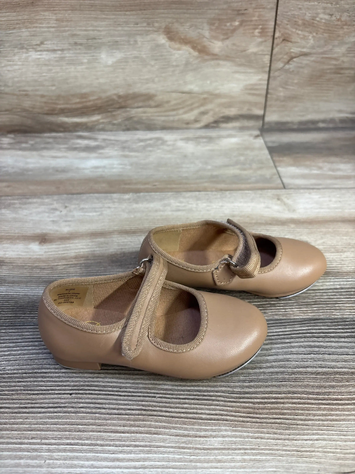 Three-quarter view of tan tap shoes in size 7C showcasing rounded toes and strap details on a wood-look floor