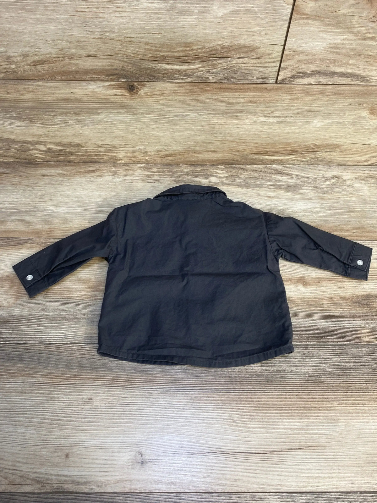 Black long sleeve button-up shirt for kids displayed flat on wooden surface