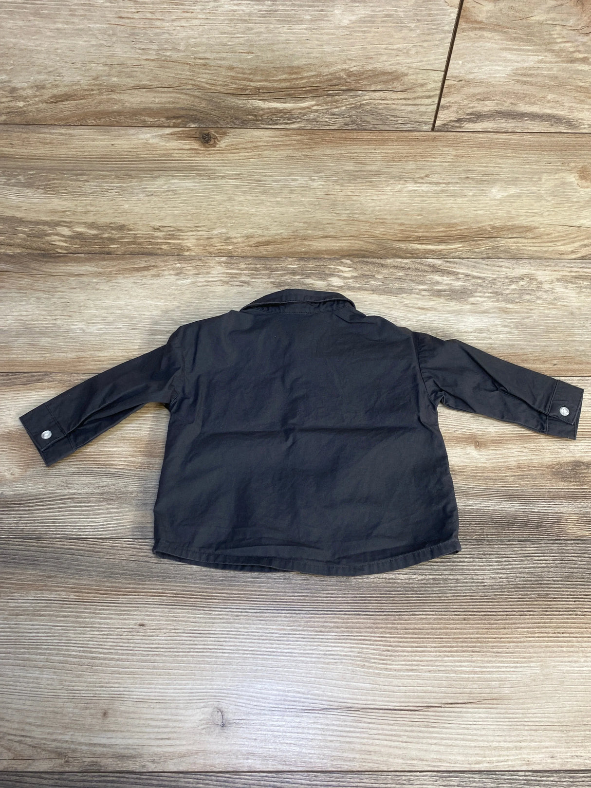 Black long sleeve button-up shirt for kids displayed flat on wooden surface