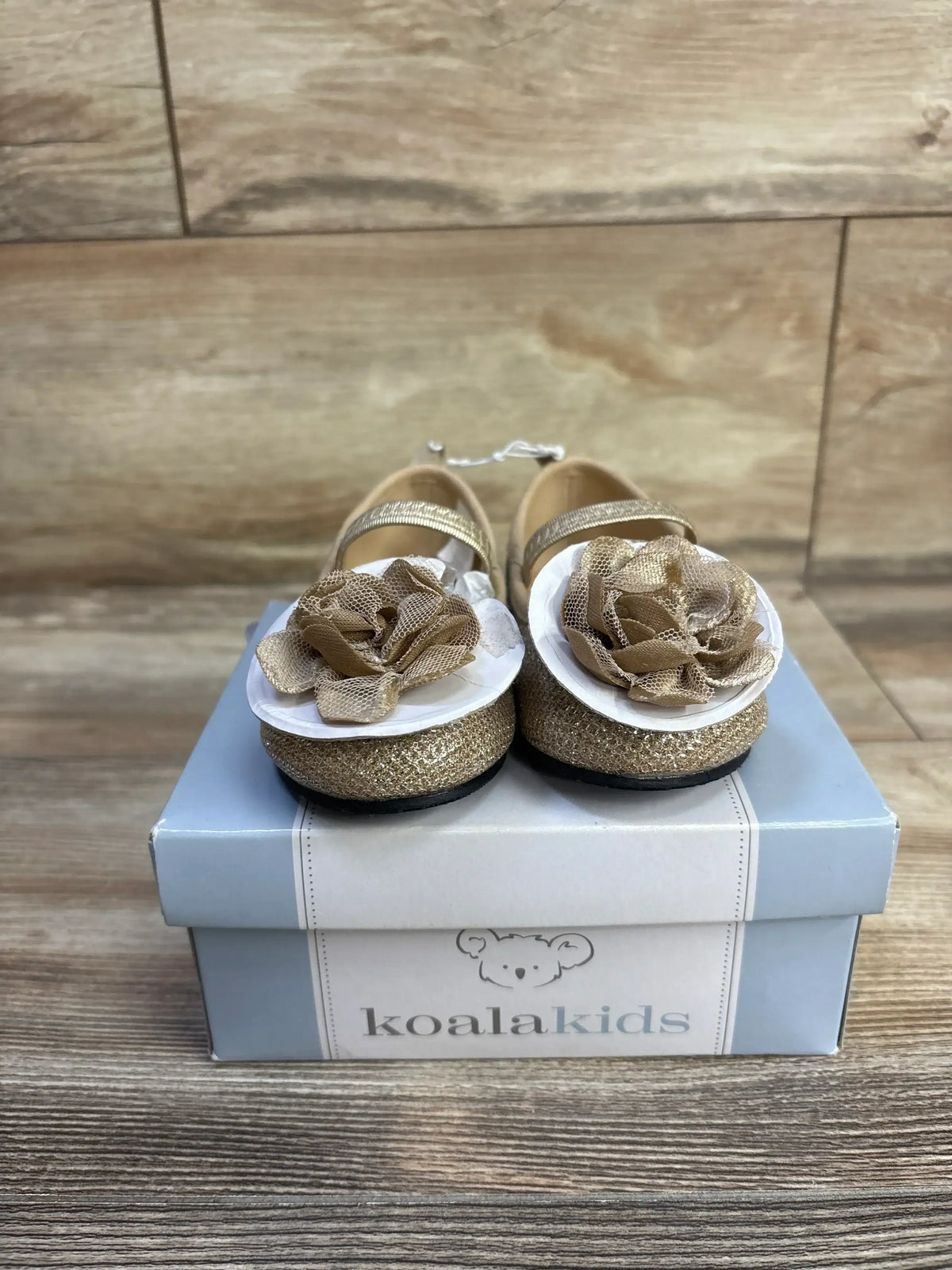 Front view of gold Koala Kids Mary Jane toddler flats with mesh flower embellishments, on a Koala Kids box on wood floor