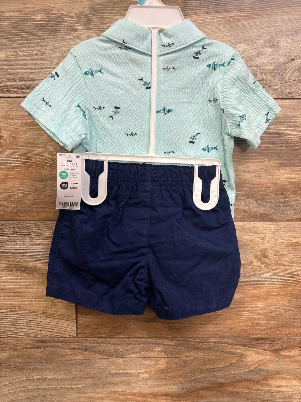 Back view of Carter's 2 piece mint green fish print button-up and navy elastic waist shorts on white hanger over wood floor