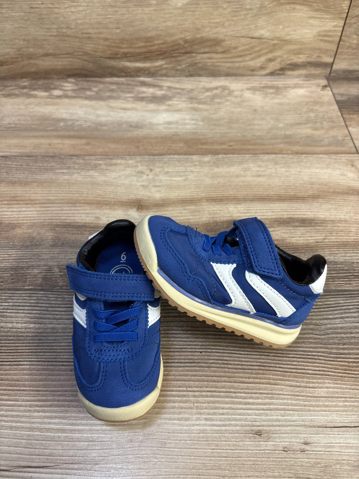 Three-quarter view of Wonder Nation blue toddler sneakers size 6C with white side stripes, velcro strap and tan sole on wood