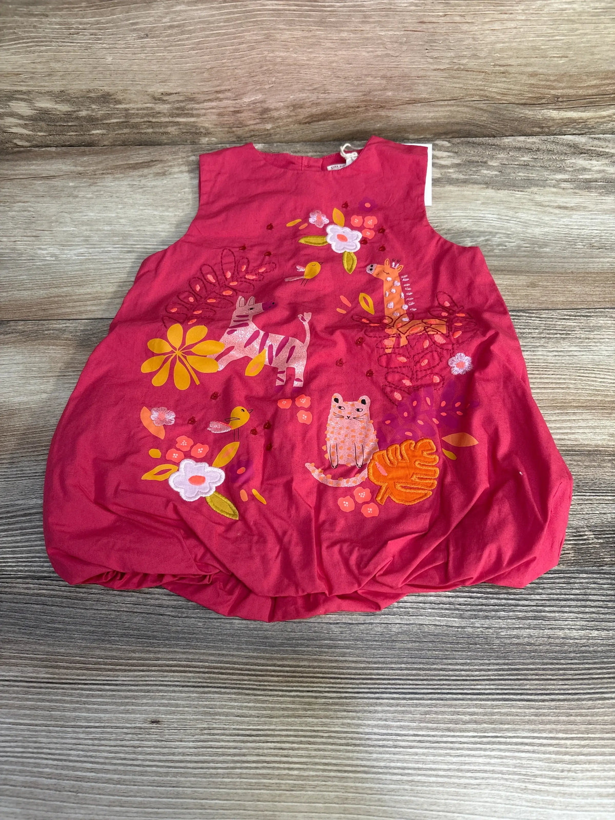 Top-down view of pink baby bouffant dress showcasing embroidered animals and flowers on a light wood floor background