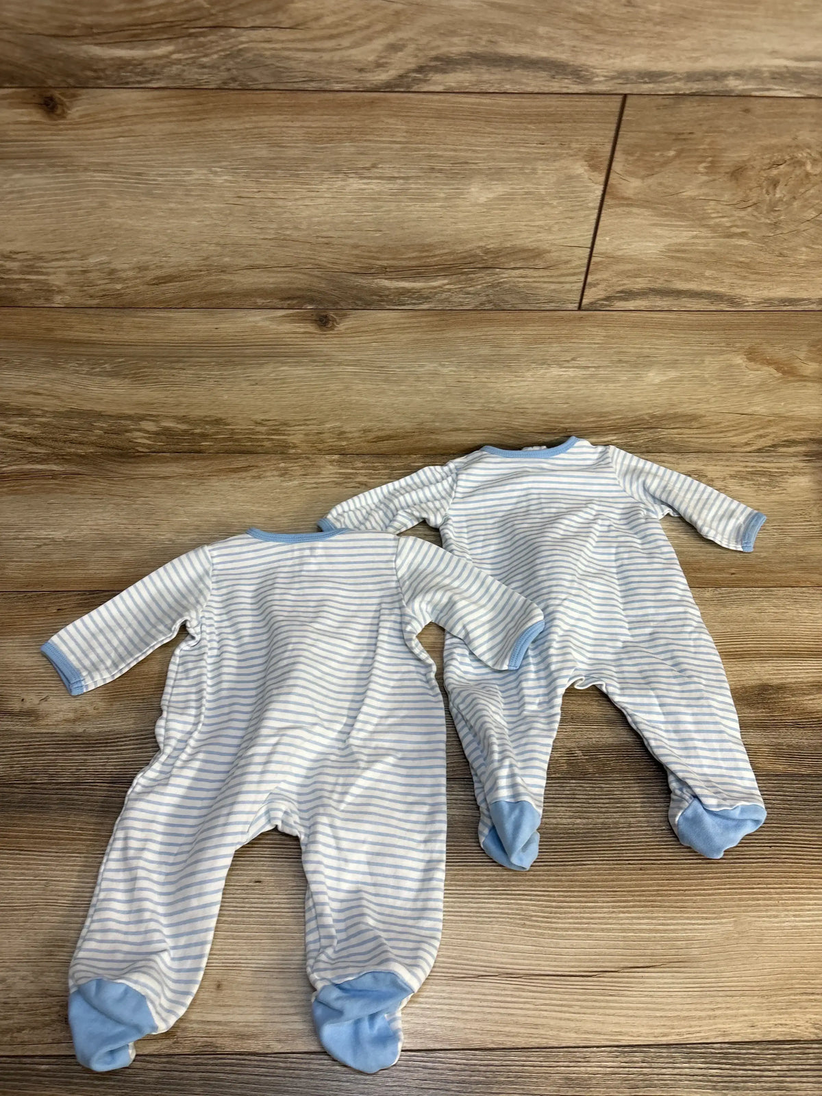 Two blue and white striped baby footed onesies on wood floor, newborn clothing