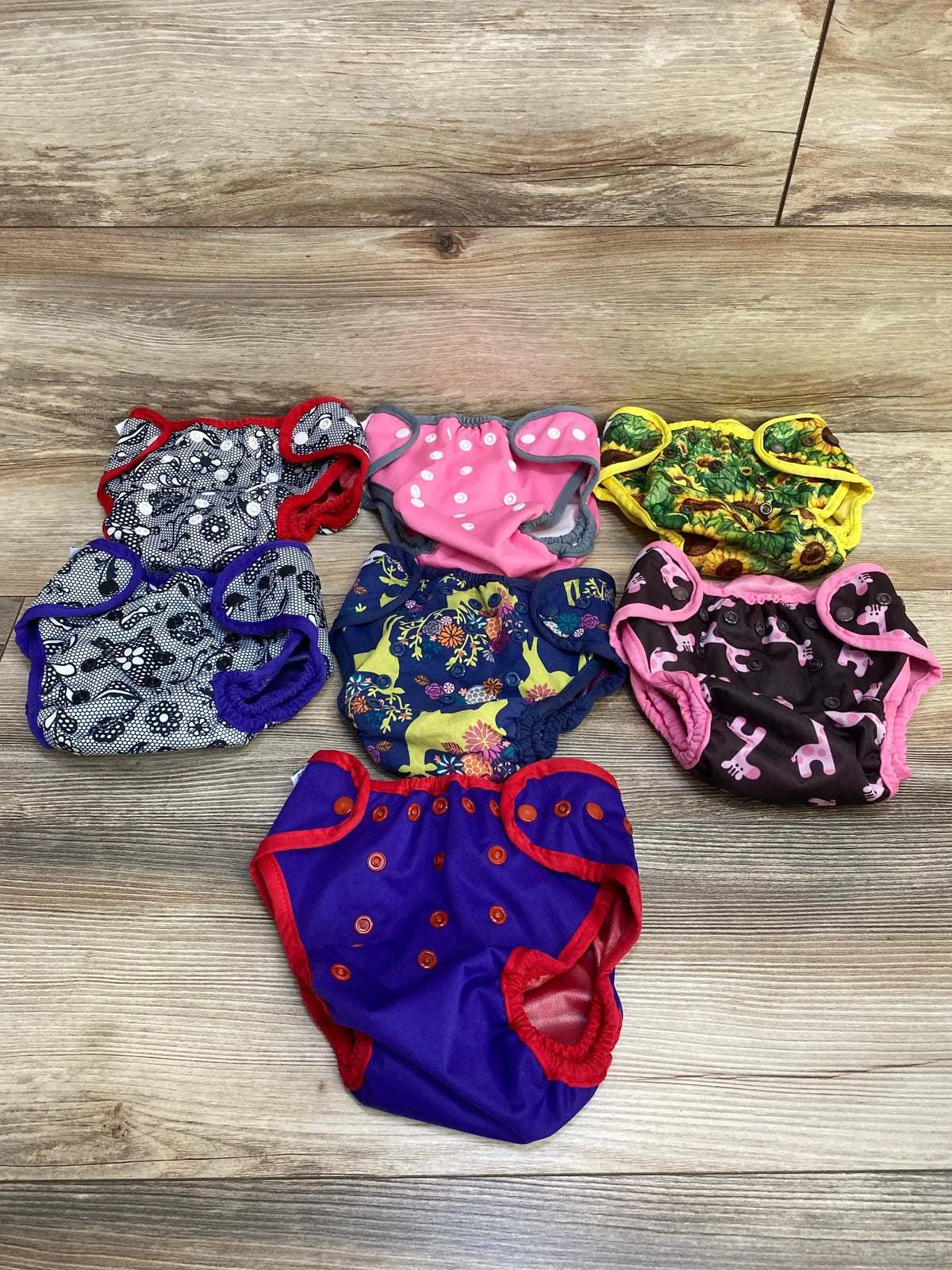 Flat lay of Best Bottom 7pk diaper covers in mixed prints with purple solid red trim and floral patterns on wood floor