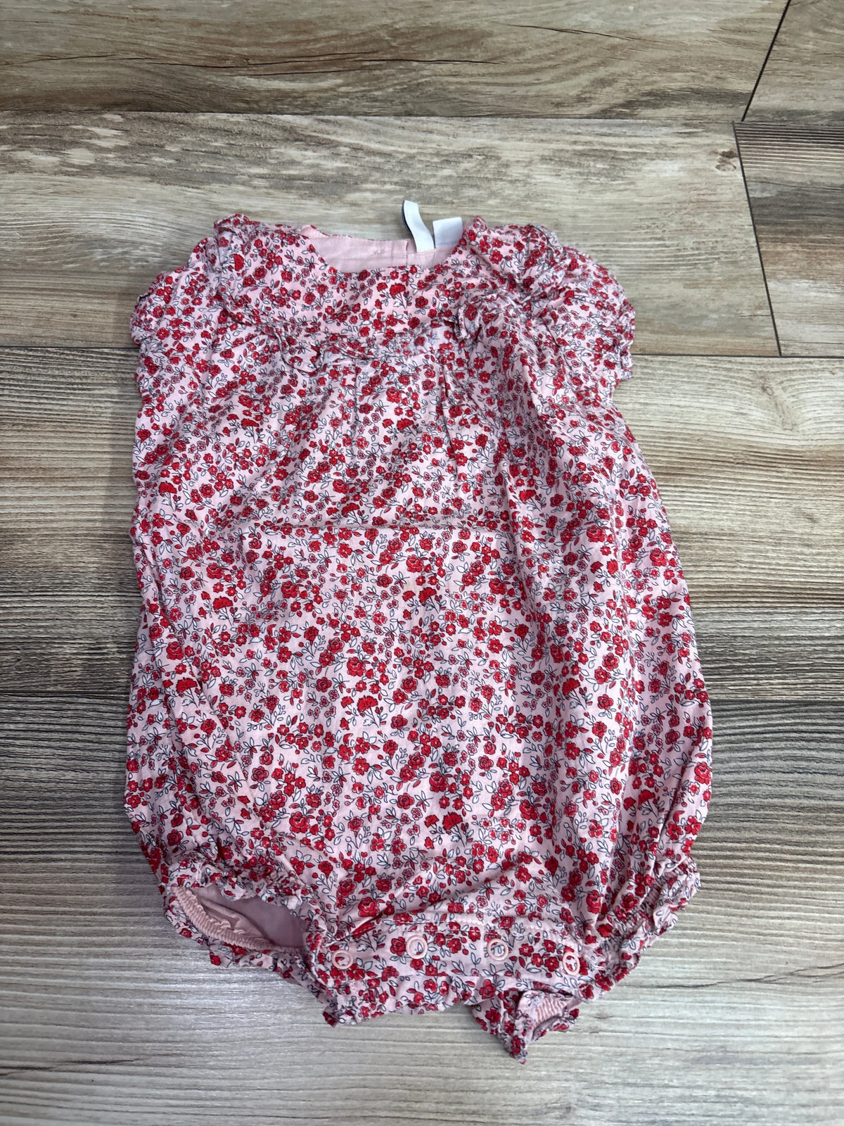 Front view of Janie & Jack pink ditsy floral ruffle romper with snap closures on a wood-grain floor