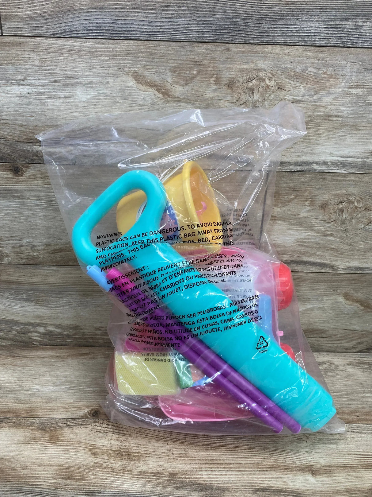 Front view of Peppa Pig cleaning trolley playset showing turquoise handle, purple poles, pink dustpan in clear plastic bag on wood background