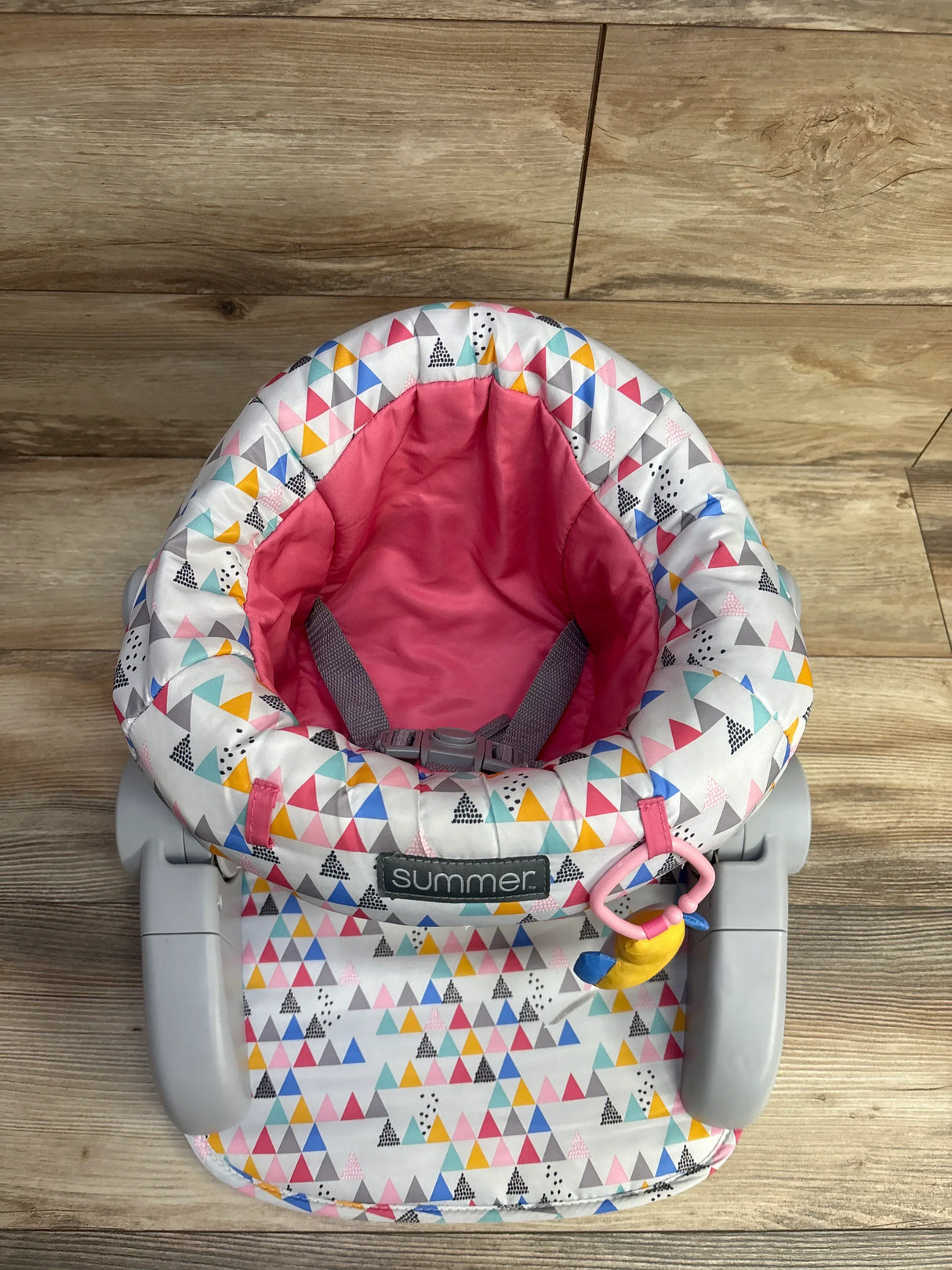 Colorful Summer baby seat with pink interior and multi-colored triangle pattern on wooden floor