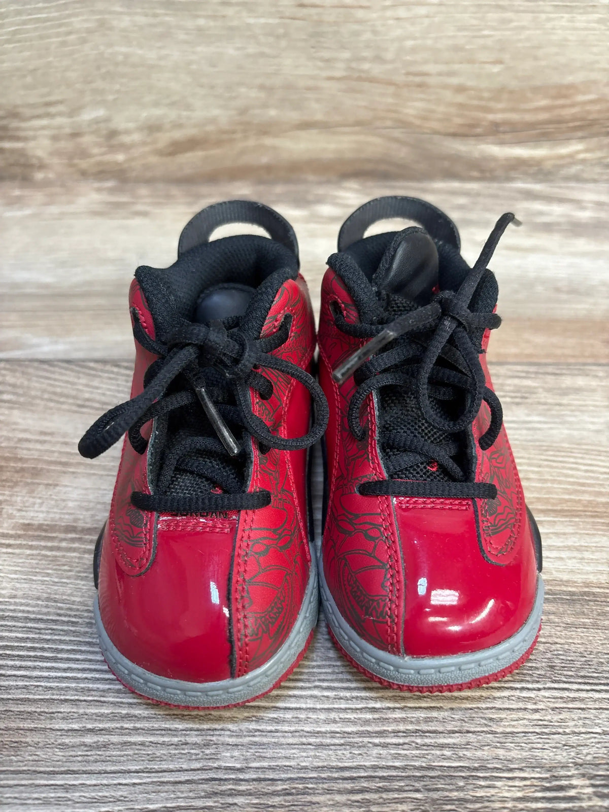 Front of Air Jordan Dub Zero toddler sneakers, glossy red patent upper, black laces, gray midsoles on wood