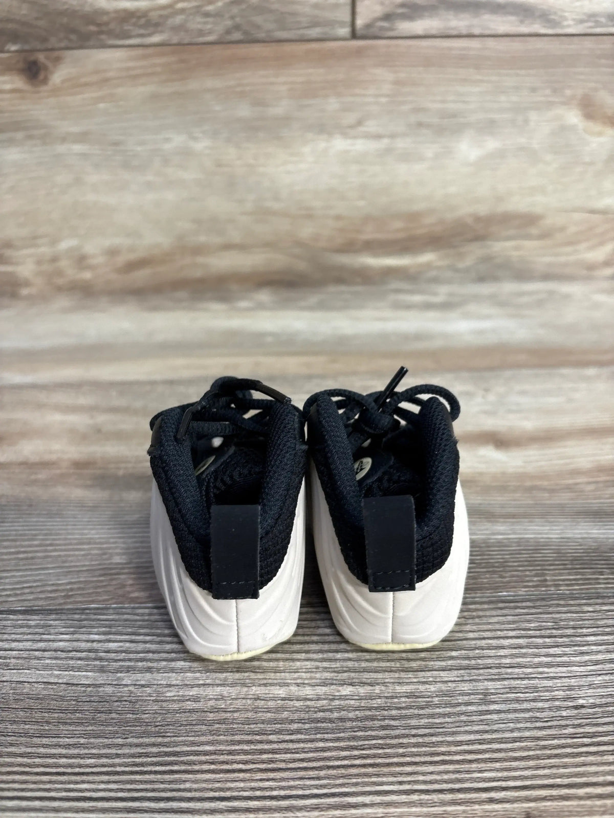 Rear view of Nike Posite One crib booties in black and white showing molded white sole and black knit upper on wood floor