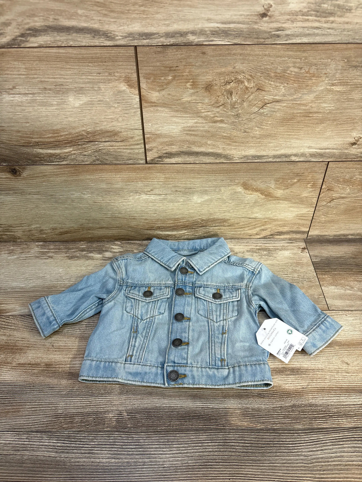 Front view of Little Co. embroidered blue denim jacket showcasing button front, chest pockets, and long sleeves on a wood background