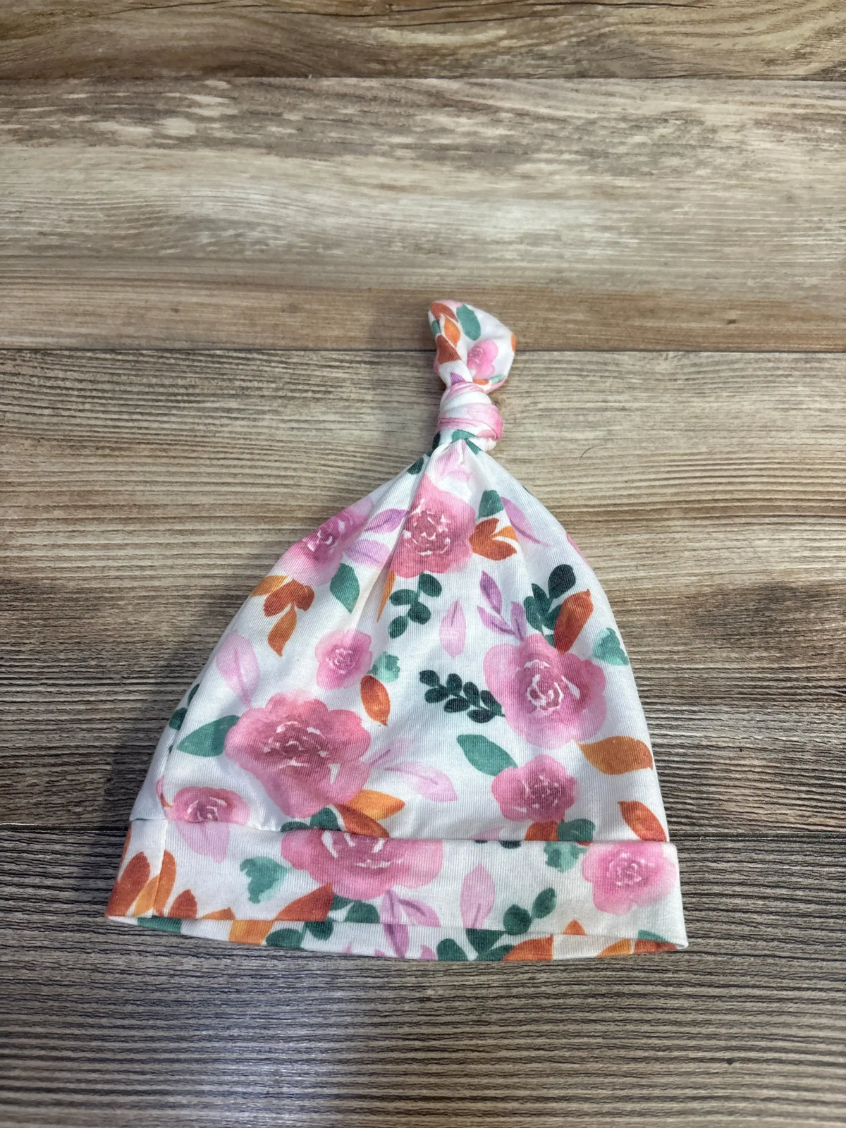 Top view of Copper Pearl Floral Top Knot Hat White showing pink floral print and knotted top on wood background