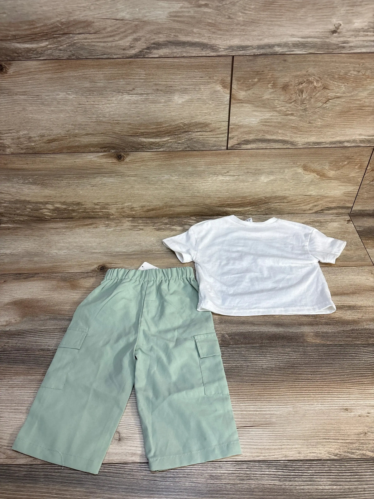 Kids mint green cargo pants and white short sleeve t-shirt on wood floor