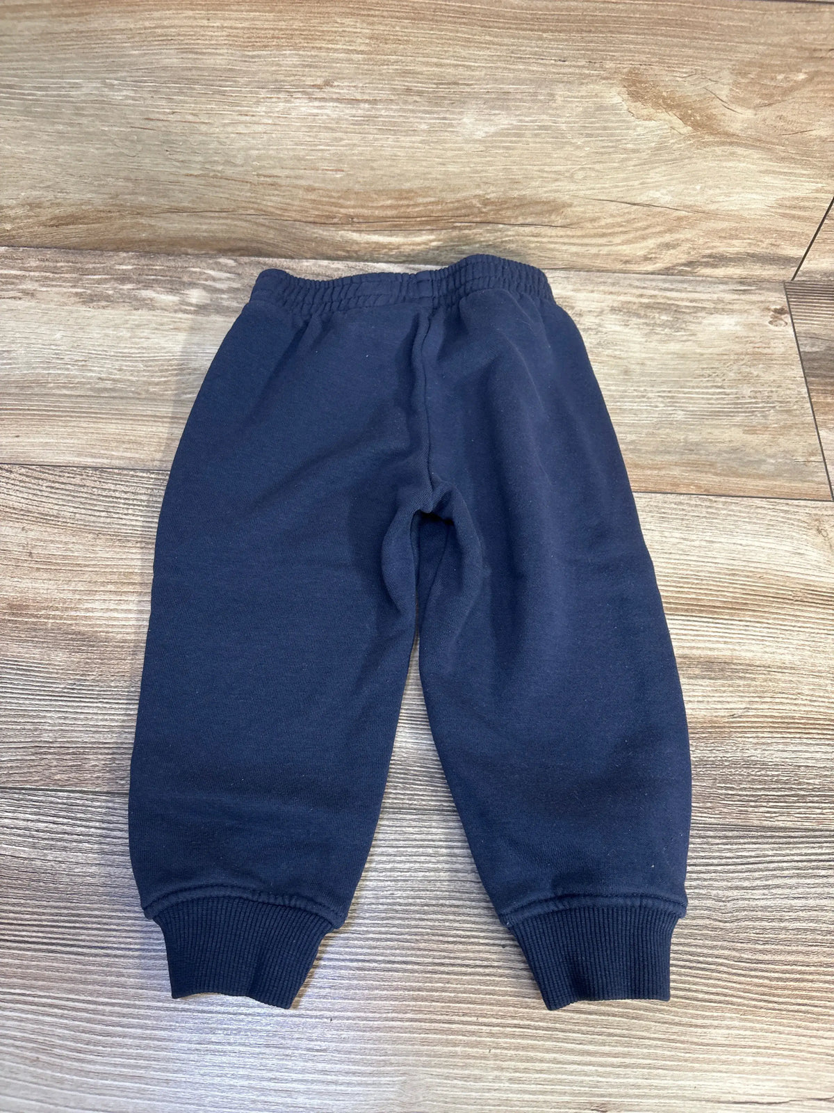 Flat lay of Champion navy joggers showcasing an elastic waistband and ribbed cuffs on a wood grain background