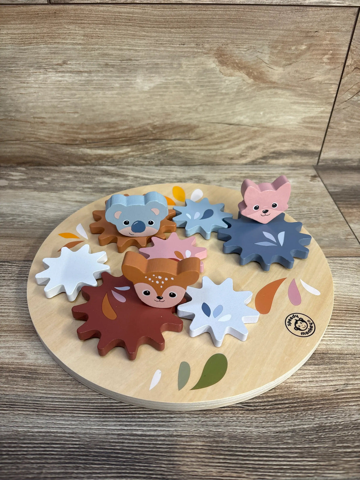 Top view of Speedy Monkey wooden gear toy with colorful animal-themed gears on a round wooden base and wood-grain background