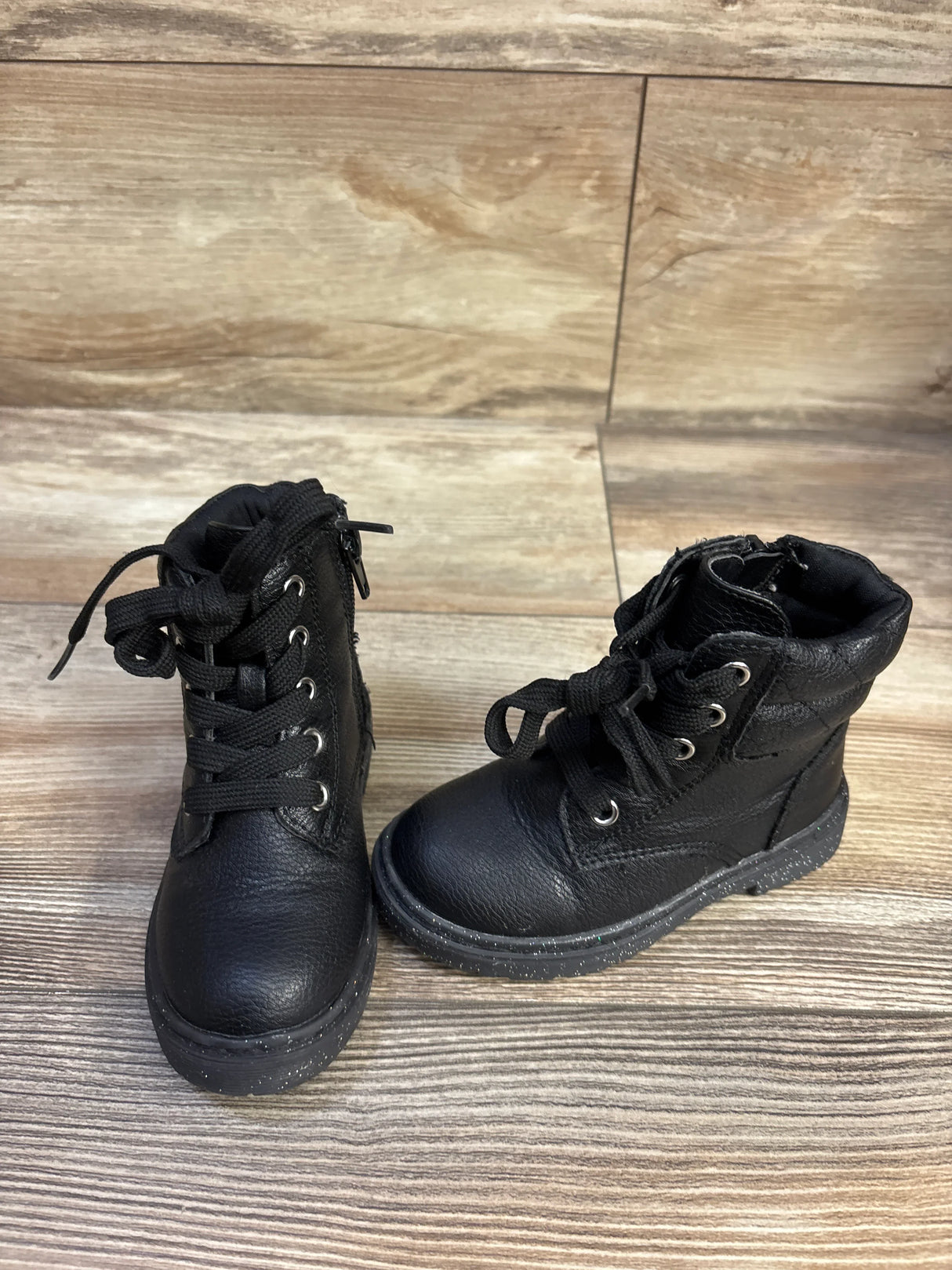 Front three-quarter view of Sincerely Jules toddler black glitter lace-up boots showcasing glitter-speckled soles on wood floor background