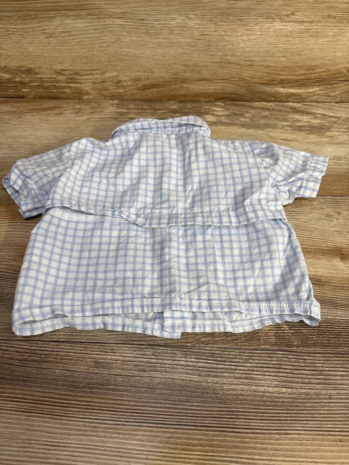 Back of Books & Bows button-up shirt in light blue gingham, size 12 months, showing short sleeves and ruffle on wood surface