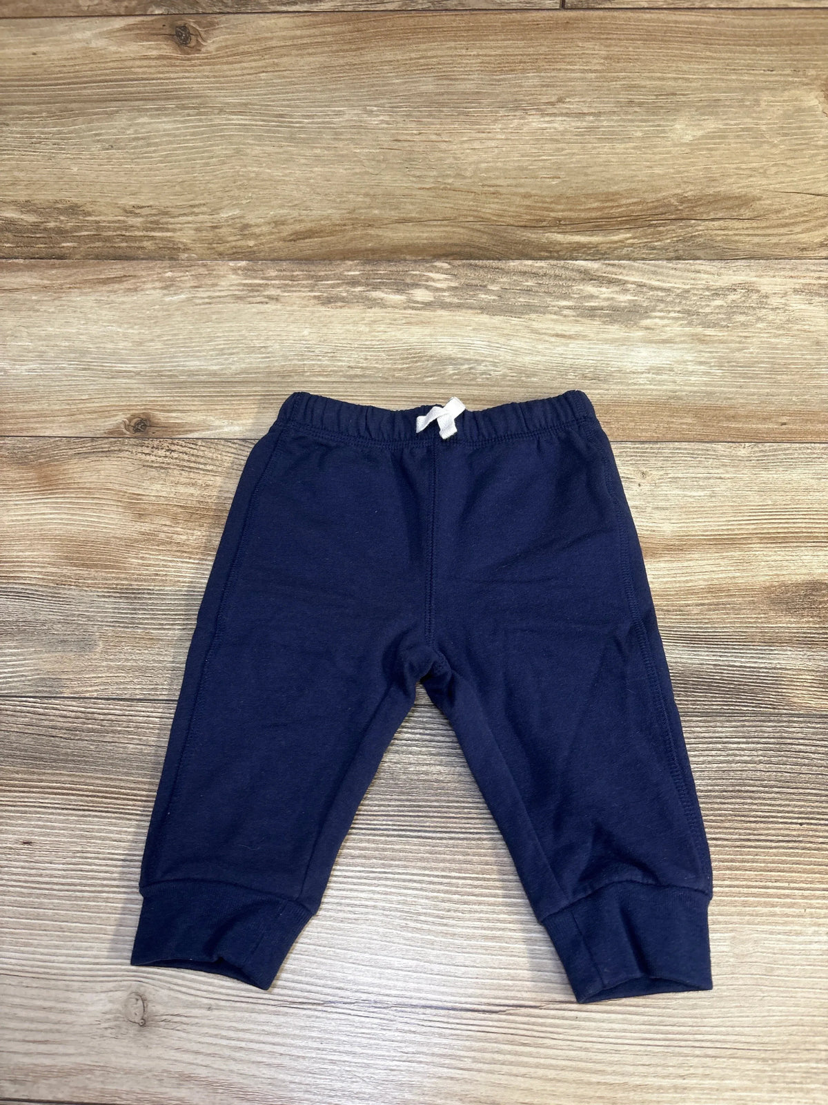 Flat lay of navy baby joggers showing elastic waistband with white tie and cuffed ankles on wood background