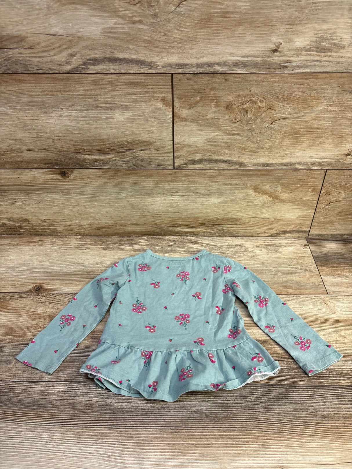 Front flat-lay of Carter’s light green long-sleeve peplum top size 2T showing pink floral print and ruffled hem on wood floor