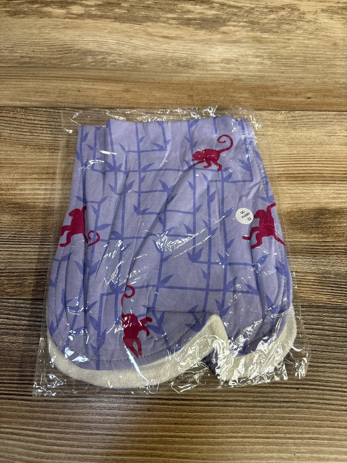 Top view of Kickee Pants burp cloth folded, lilac bamboo-grid print with red monkeys, white terry trim, in clear wrap on wood