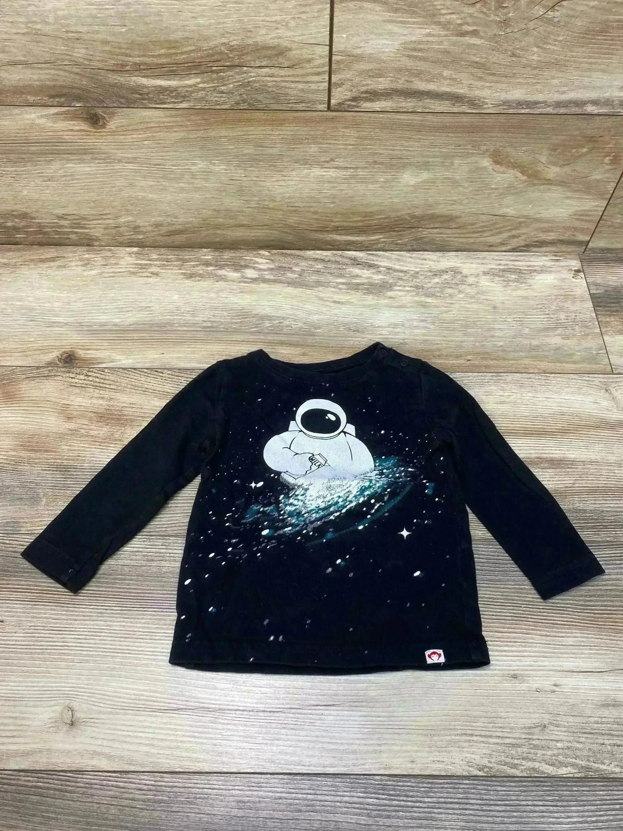 Flat-lay of black Appaman Space Milk toddler long-sleeve tee with white astronaut graphic on wood background