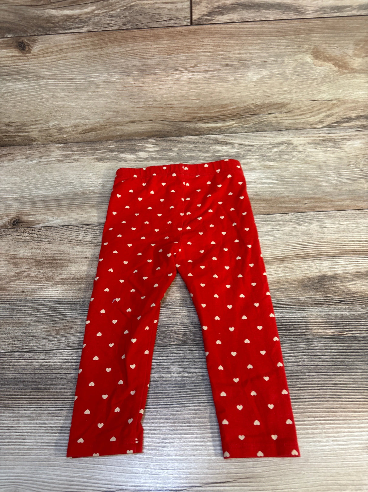 Red toddler leggings with white heart print on wood floor